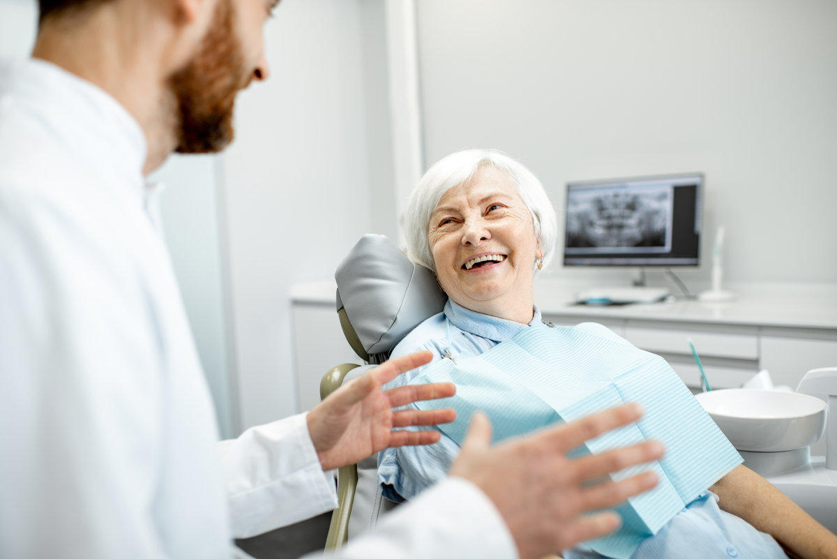 Beautiful elder woman with healthy smile sitting during the consultation with dentist at the dental office