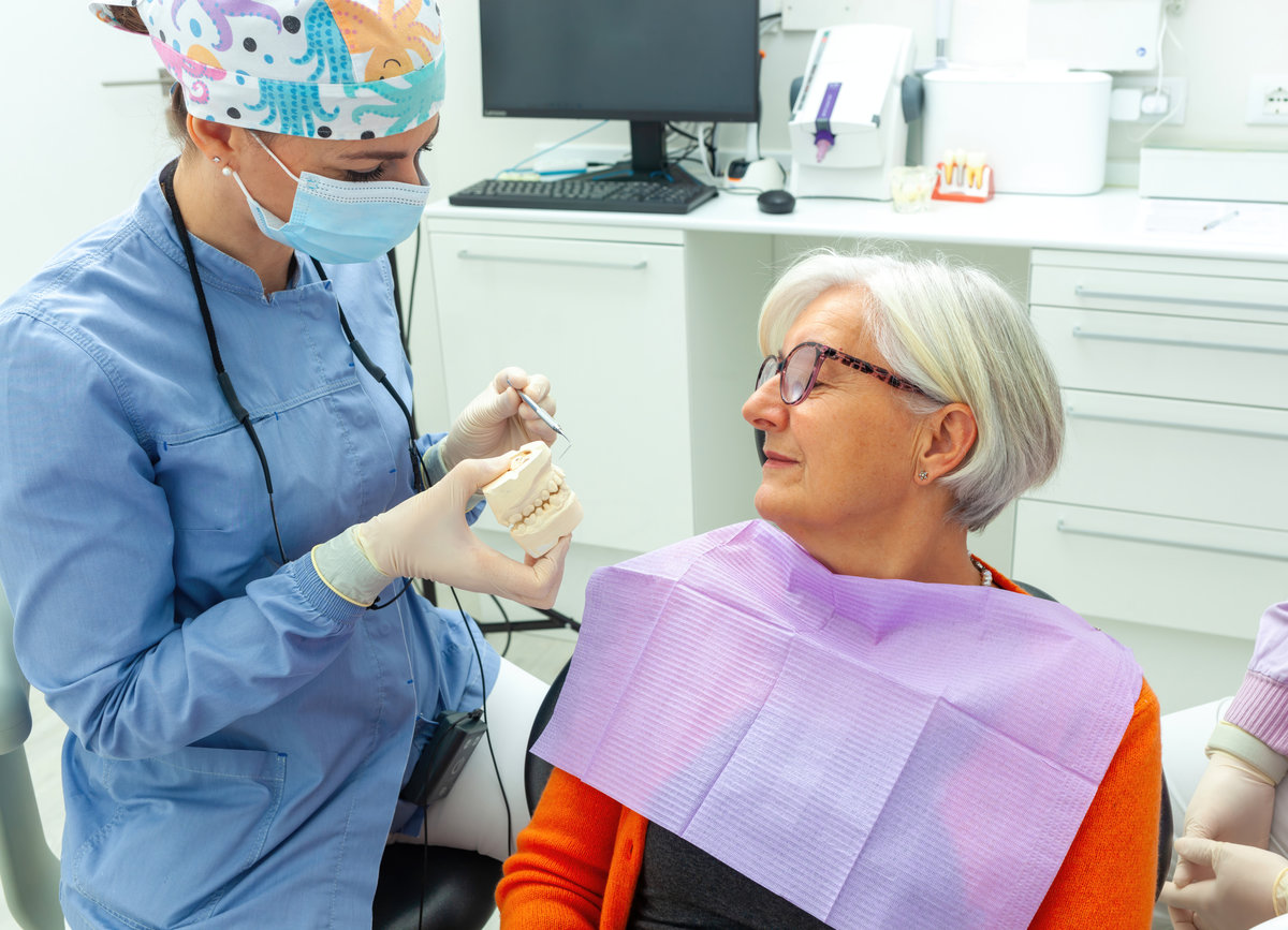 Dentist explaining dental treatment to senior woman while using a denture model in a welcoming clinic environment