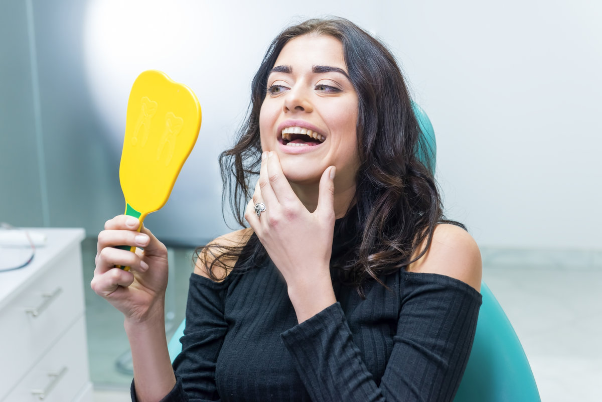 Lady looking at her teeth. Woman holding mirror, dentist office.