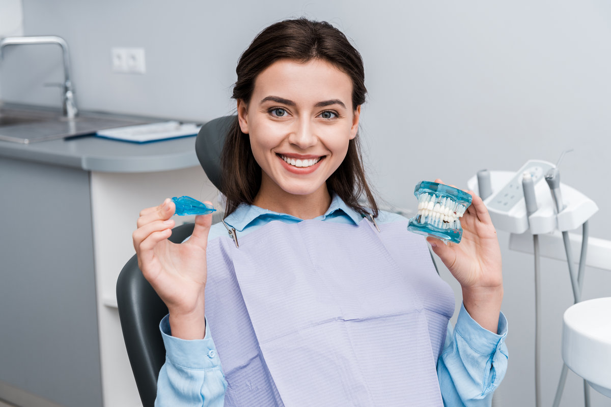 cheerful young woman holding teeth model and retainer in hands