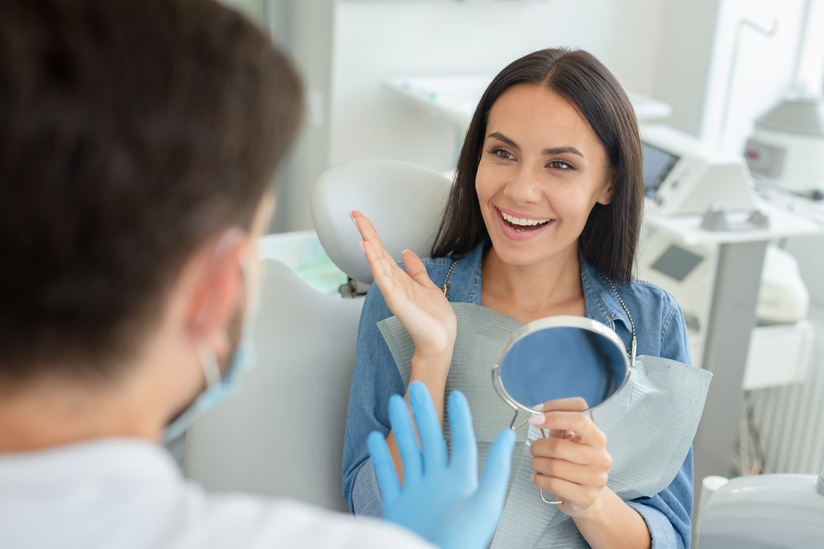 male dentist and happy gesturing client holding mirror talking in dental office