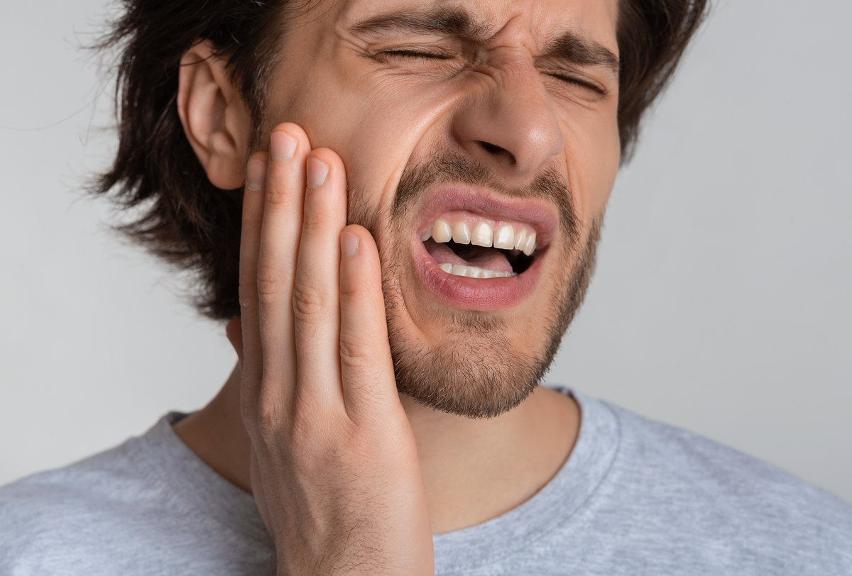 Young male feeling tooth pain, holding cheek with hand