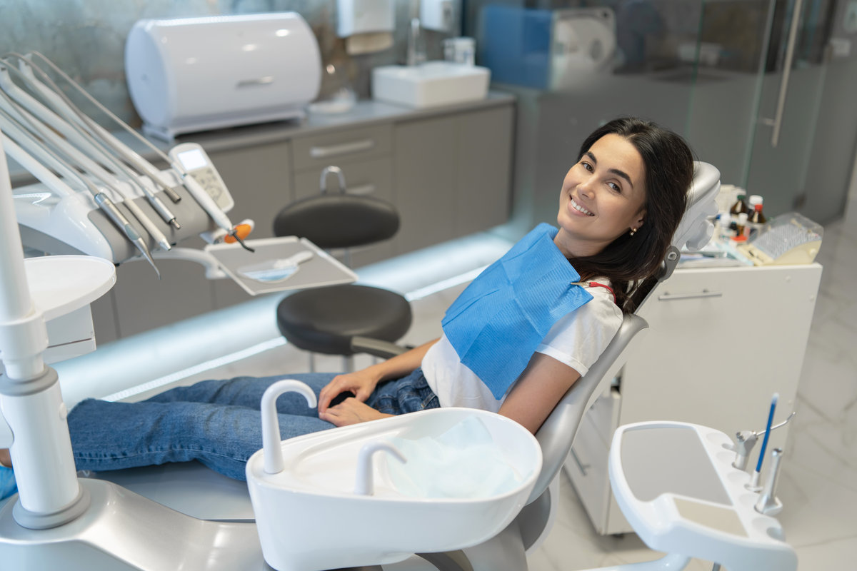Pretty brunette happy female patient sitting in the chair at dental clinic