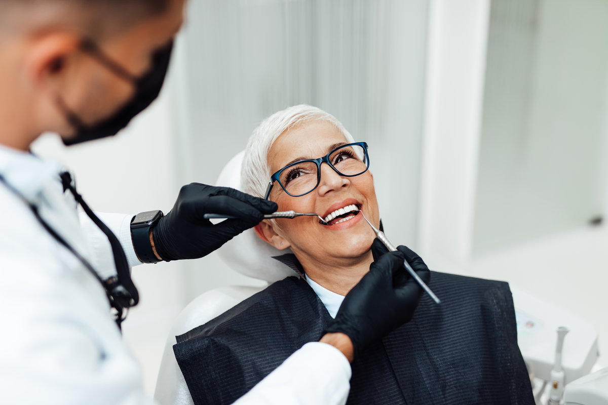 Beautiful senior woman having dental treatment at dentist's office. Dentist is wearing protective face mask due to coronavirus pandemic.