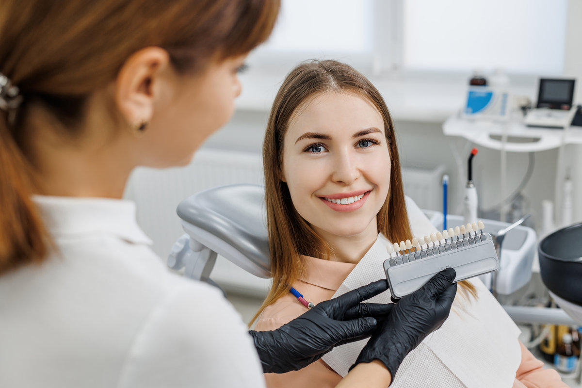 Dentist demonstrate for patient teeth color shades guide for tooth whitening. Teeth color matching samples for implants or veneers in doctor hands. Concept photo on dental theme.