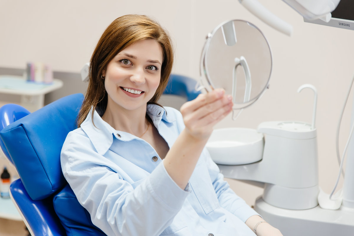 young woman smiling with healthy white teeth, looking in dental mirror