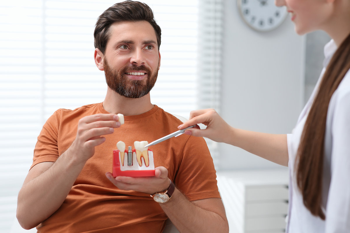 Doctor with educational model of dental implant consulting patient in clinic