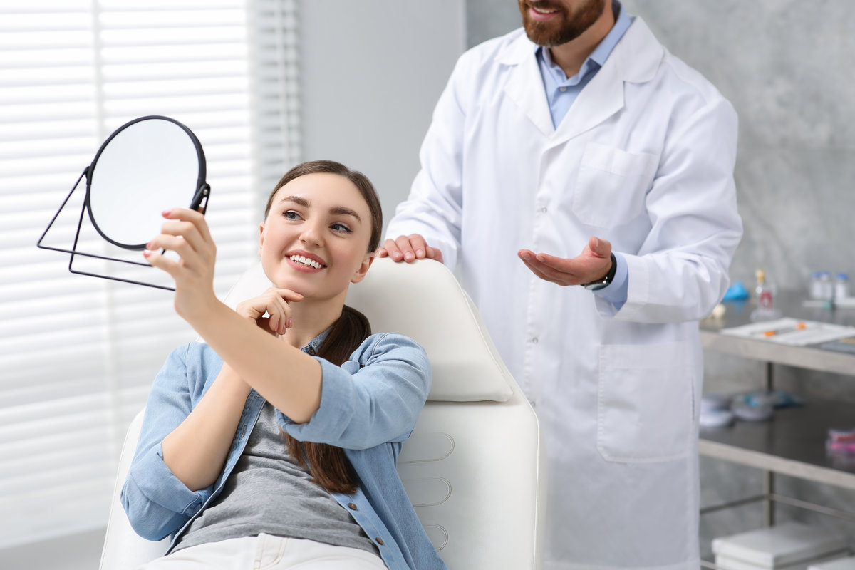 Young woman looking at her new dental implants in mirror indoors