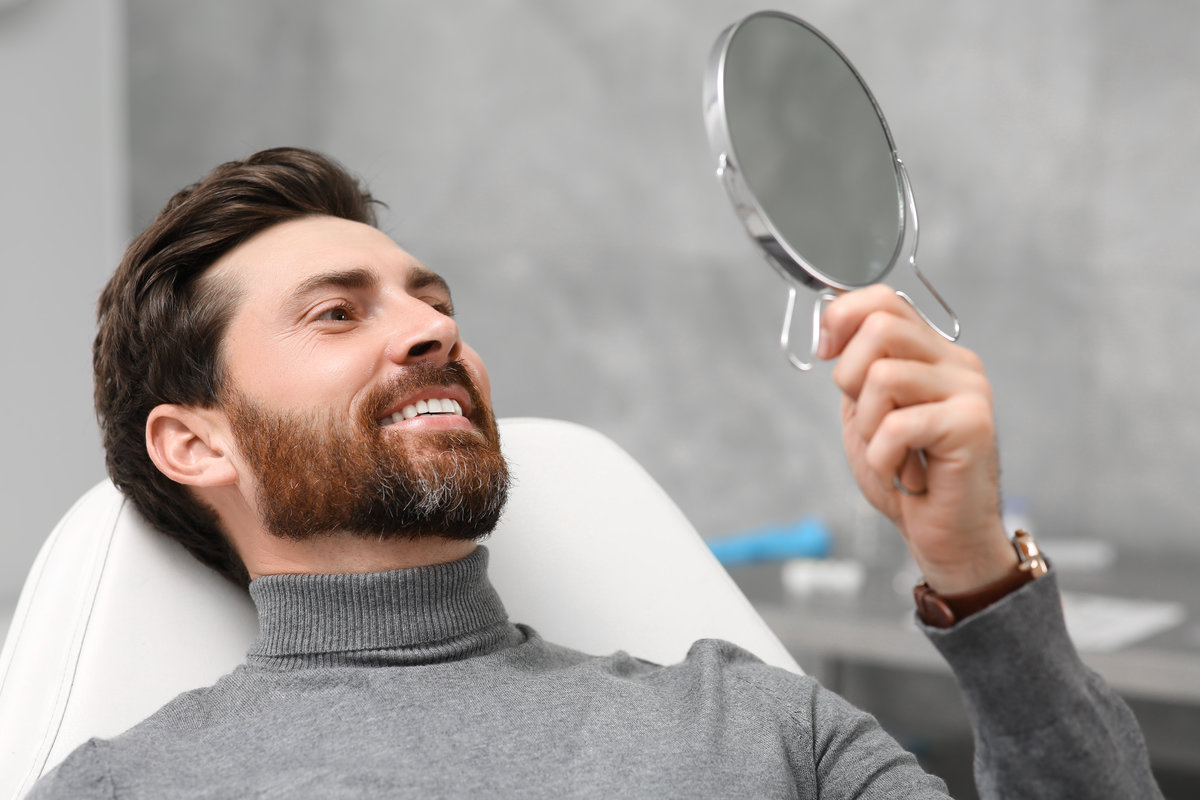 Man looking at his new dental implants in mirror indoors