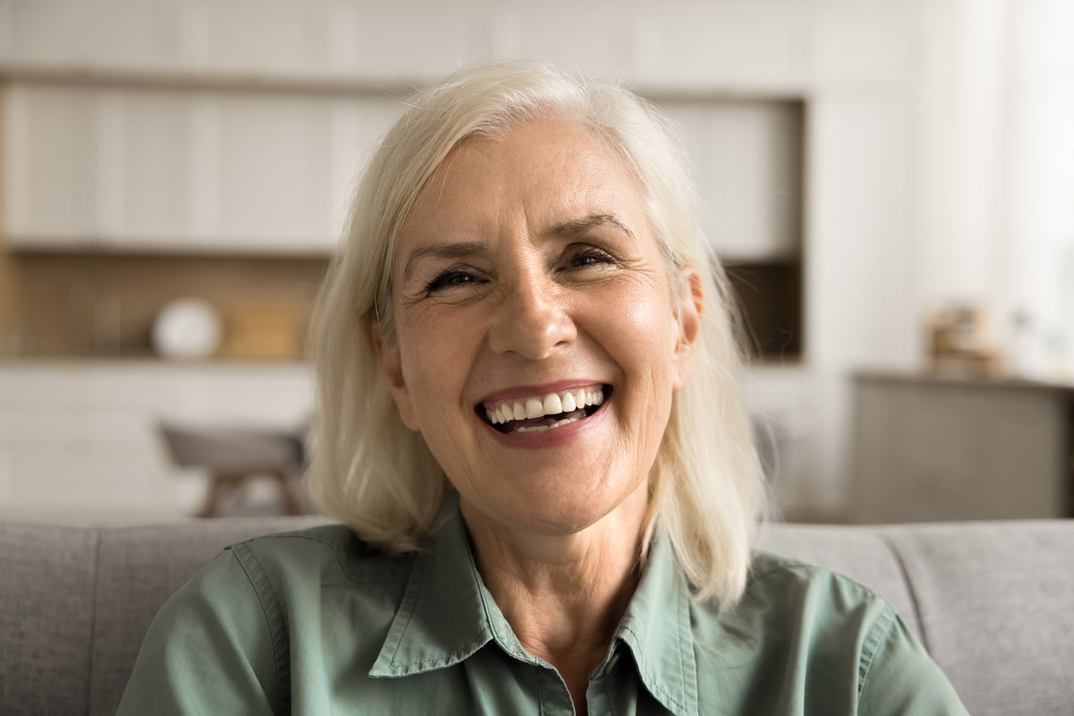 Joyful positive senior woman close up front head shot portrait. Happy blond old lady looking at camera with beautiful toothy smile, laughing, talking on video conference call at home